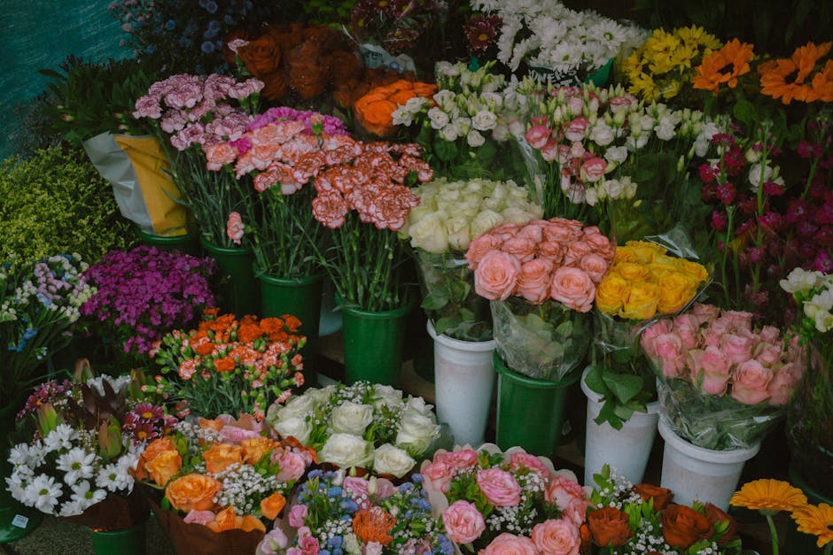 A vibrant display of fresh floral arrangements arranged in various bouquets, with roses in shades of pink, yellow, and white, alongside purple, white, and orange carnations, daisies, and other mixed f