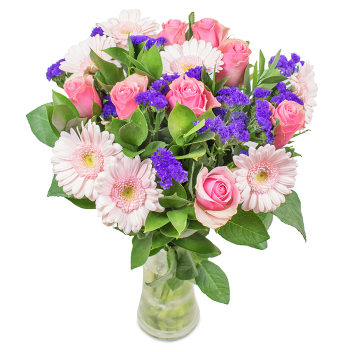 A striking and elegantly arranged floral bouquet sits in a sleek clear glass vase, set before a crisp white background-its blooms a celebration of pinks and violets reminiscent of Hither Green's spring festivals. The centerpiece glows with approximately eight soft pink roses, tightly wound or just beginning to unfurl, their spiral petals embodying classic beauty and gentle romance. Nestled beside them are half a dozen pastel pink Gerbera daisies, their open faces and delicate white-edged centers gleaming softly. Throughout the bouquet, clusters of vibrant purple statice capture the eye and introduce both texture and a playful note of brightness. All are interlaced with a base of lush, deep green foliage, whose rich colour and subtle scent evoke the freshness of local parks after rain. The transparent vase, revealing the stems and clear water, completes the freshness and natural equilibrium of the arrangement. Ideal for birthdays, anniversaries, or to add a charming, local touch to a Hither Green workspace or home, this artful design-skillfully prepared by Hither Green Florist-conveys joy, celebration, and a sense of genuine community affection.